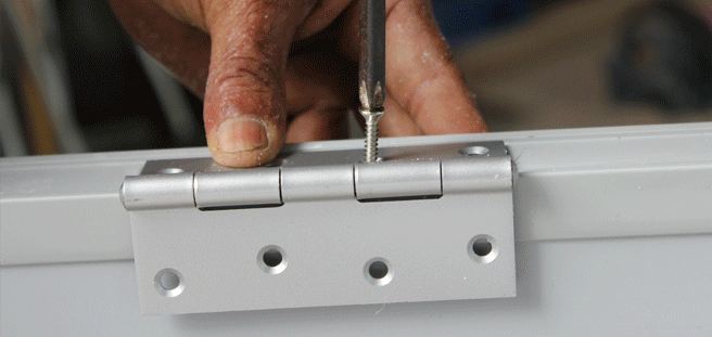 hand holding a screw driver screwing a hinge to a door