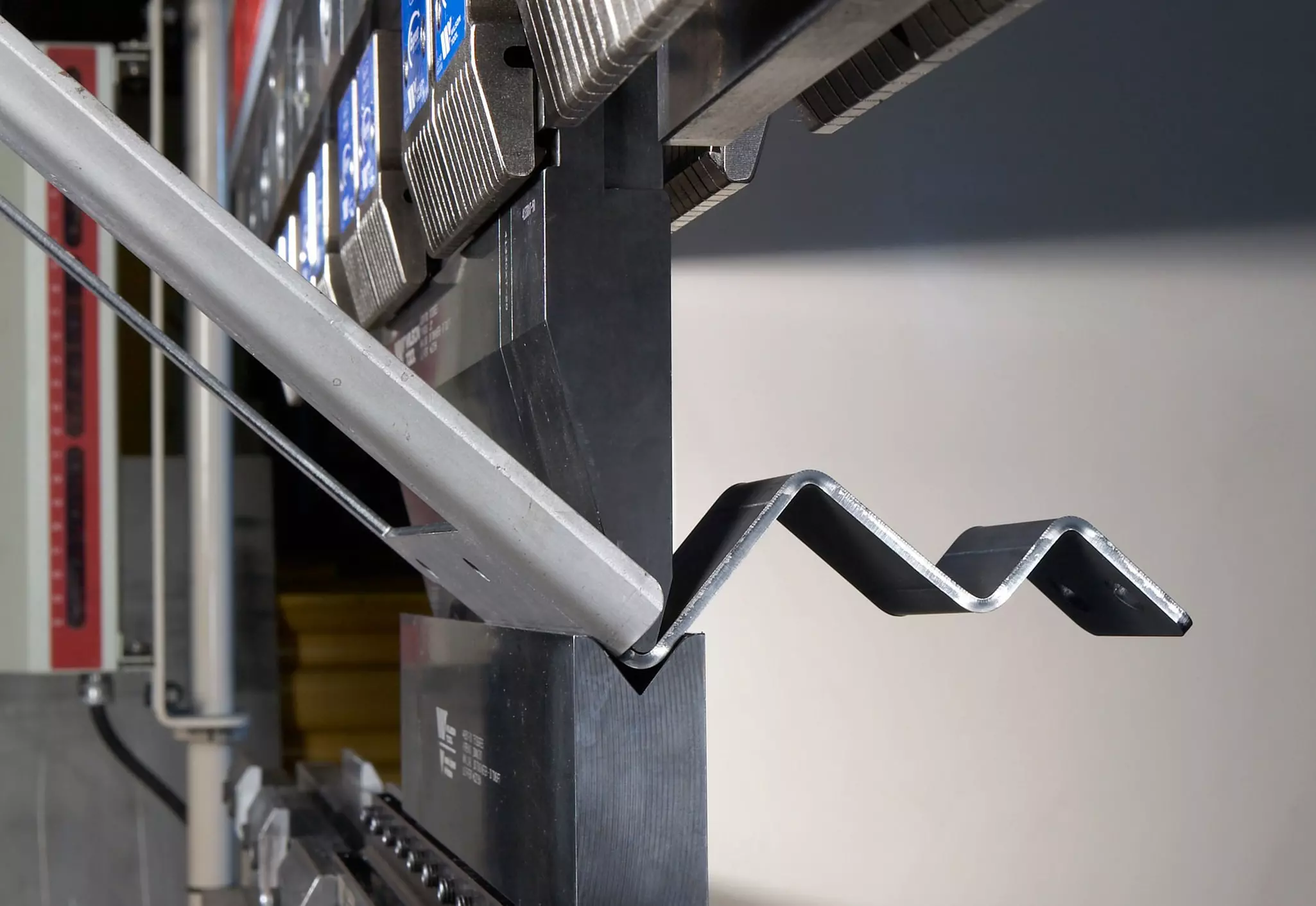 Primer plano de metal doblado en forma de zigzag con una prensa plegadora al fondo
