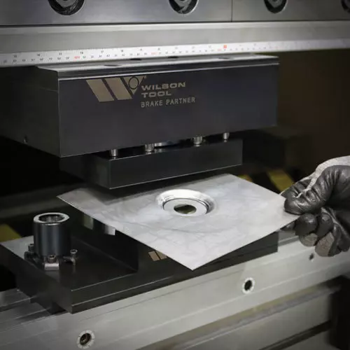 Press brake with operator holding a emboss metal sample on black image